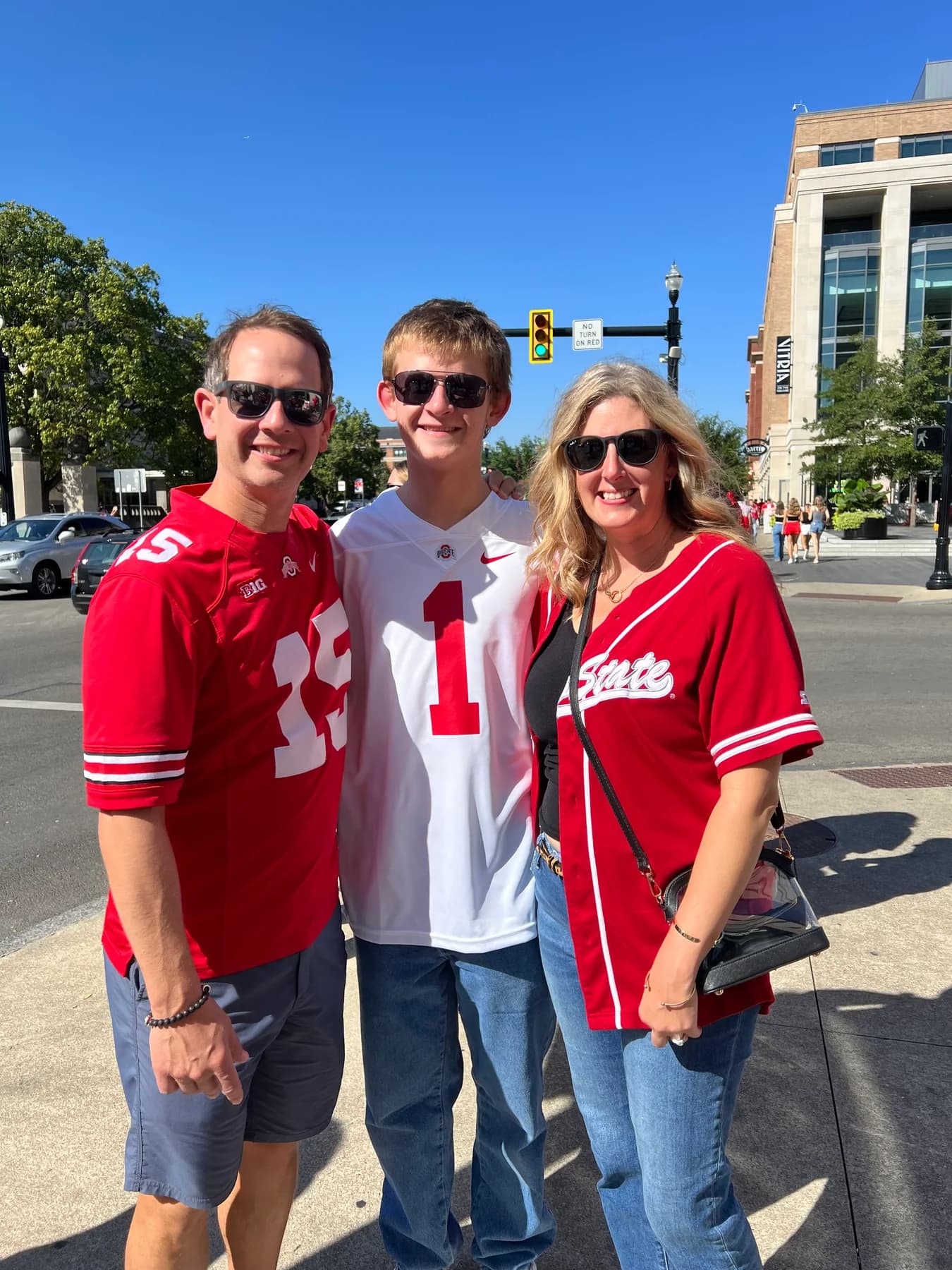 Three people in red and white football jerseys on a sunny street